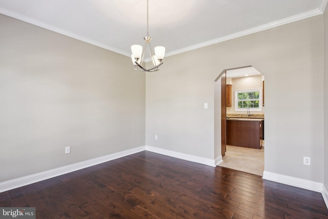 empty room with arched walkways, ornamental molding, dark wood-style floors, baseboards, and a chandelier