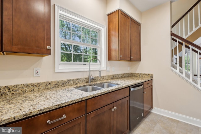 kitchen with a sink, dishwasher, baseboards, and light stone countertops