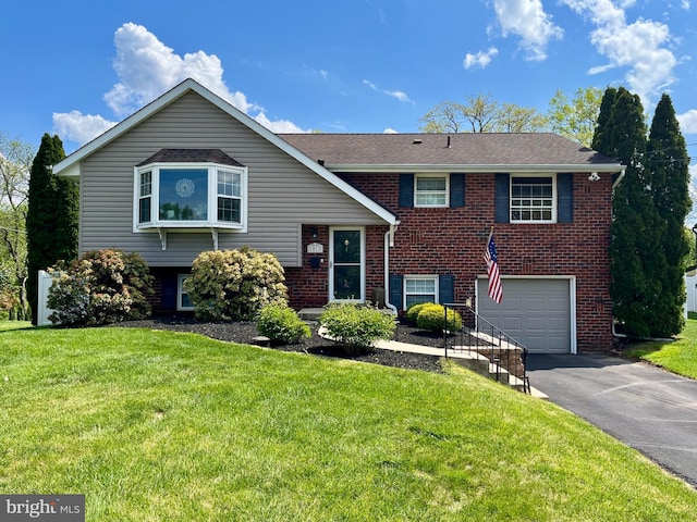 view of front of home with an attached garage, asphalt driveway, brick siding, and a front yard