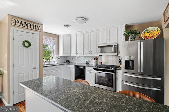 kitchen with appliances with stainless steel finishes, a sink, white cabinetry, backsplash, and dark wood-type flooring