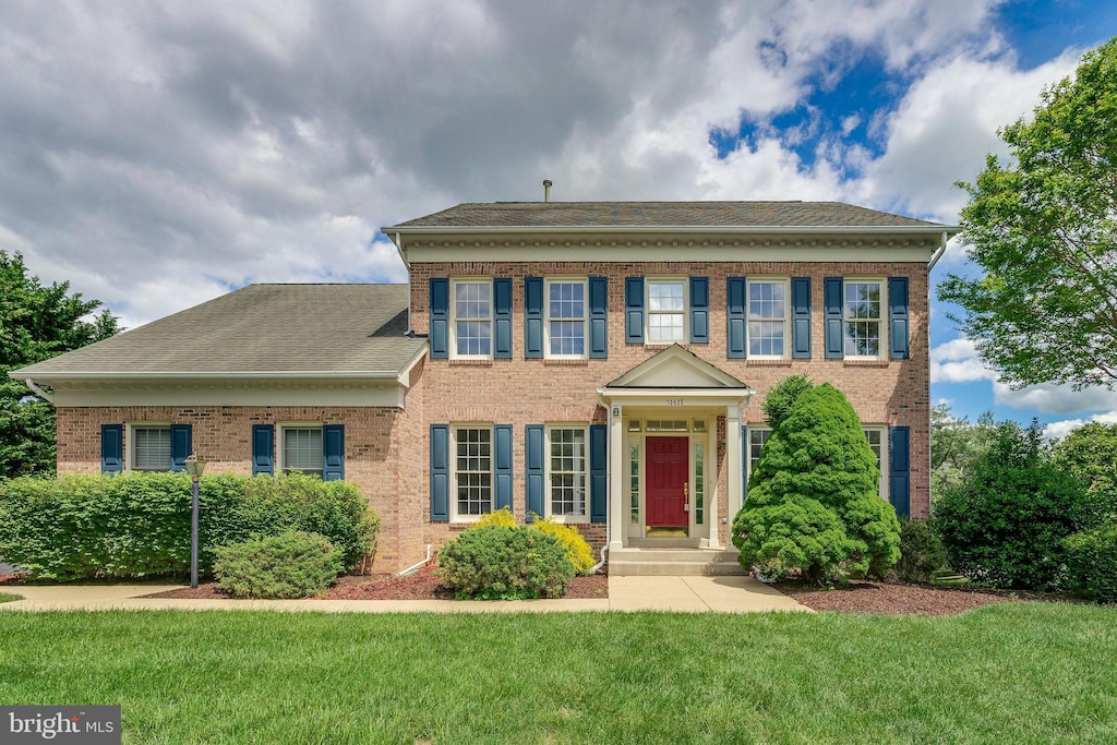 colonial-style house featuring brick siding, a front yard, and a shingled roof