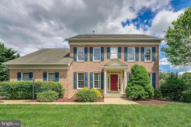 colonial-style house featuring brick siding, a front yard, and a shingled roof
