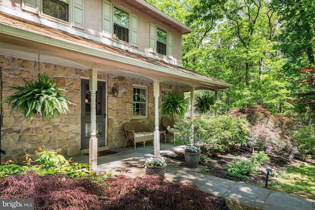 view of exterior entry featuring a porch, stone siding, and stucco siding