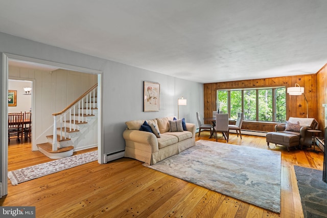 living room with baseboard heating, wood-type flooring, stairway, wood walls, and a chandelier