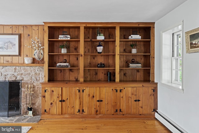 detailed view of baseboard heating, wood finished floors, and a stone fireplace