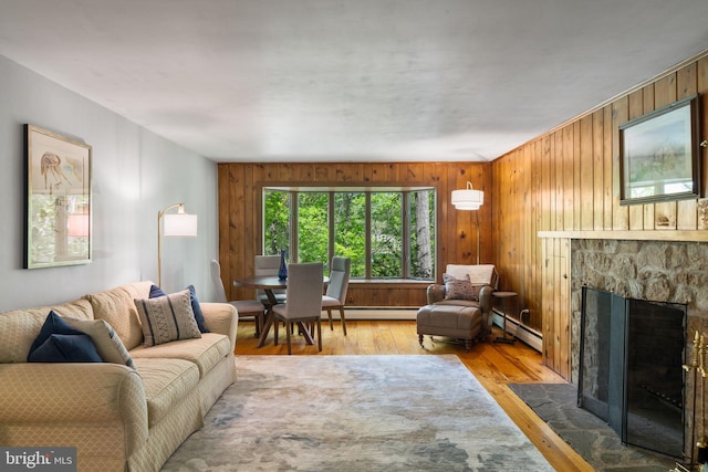 living area featuring a baseboard radiator, a stone fireplace, wood finished floors, and wooden walls