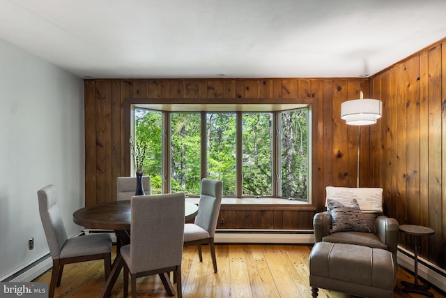 dining room with a baseboard radiator, light wood finished floors, wooden walls, and baseboards
