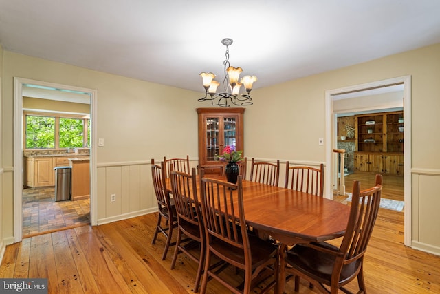 dining space featuring light wood-style flooring, a chandelier, and wainscoting