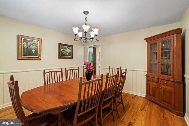 dining room with a chandelier, a wainscoted wall, light wood-style floors, and a decorative wall