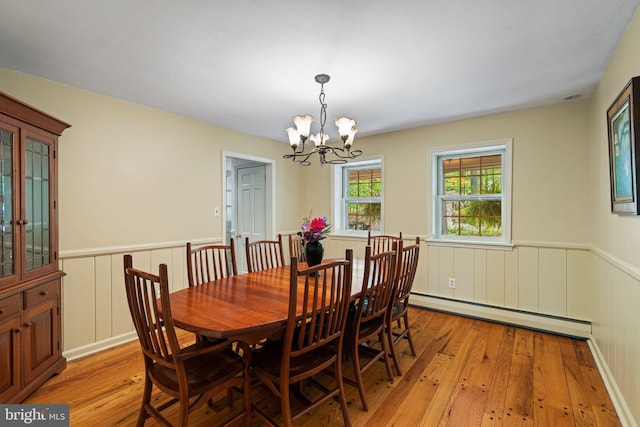 dining area featuring a baseboard heating unit, light wood-type flooring, a wainscoted wall, and a chandelier