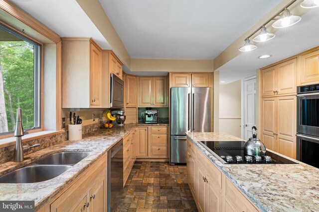 kitchen with appliances with stainless steel finishes, a sink, stone finish floors, and light brown cabinetry