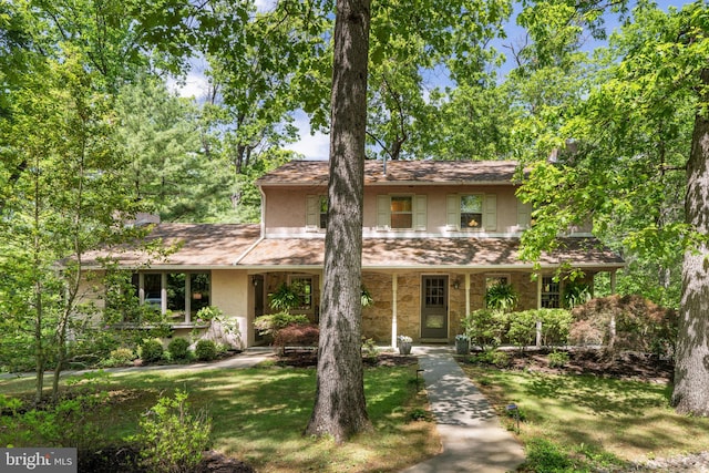 view of front facade featuring stucco siding, a front lawn, stone siding, and covered porch