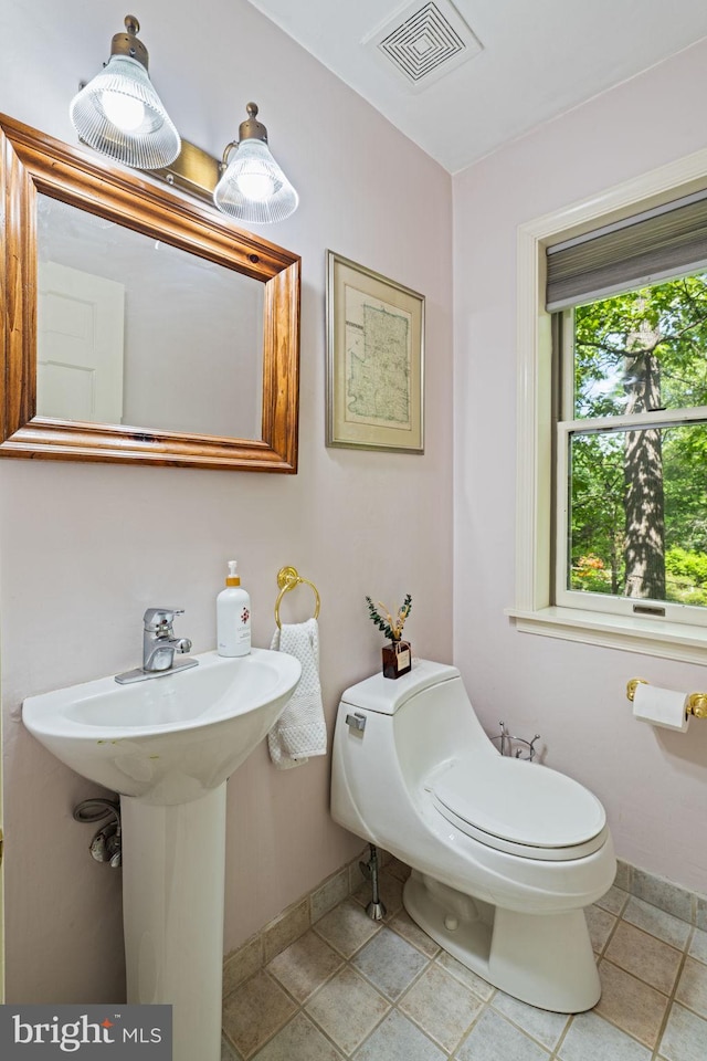 half bathroom with baseboards, toilet, and a sink