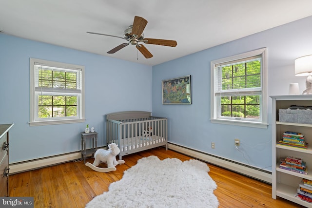 bedroom featuring a baseboard heating unit, multiple windows, a nursery area, and wood finished floors
