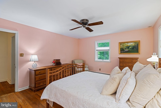 bedroom featuring hardwood / wood-style floors, baseboards, a ceiling fan, and a baseboard heating unit