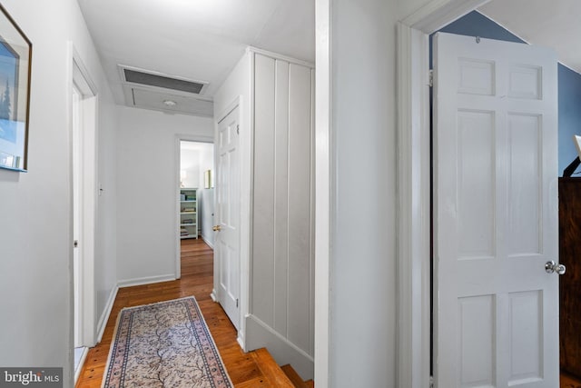 hall with attic access, light wood-type flooring, and baseboards
