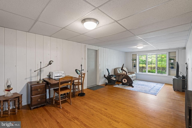workout area featuring light wood finished floors and a drop ceiling