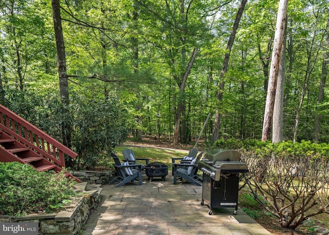 view of patio featuring a fire pit, a grill, a wooded view, and stairway