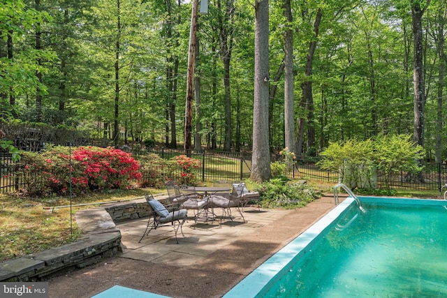 view of swimming pool with a patio area, a fenced backyard, a forest view, and outdoor dining area