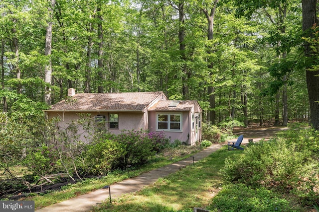 view of side of property featuring a chimney, a forest view, and stucco siding