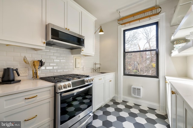 kitchen with stainless steel appliances, dark floors, baseboards, white cabinetry, and backsplash