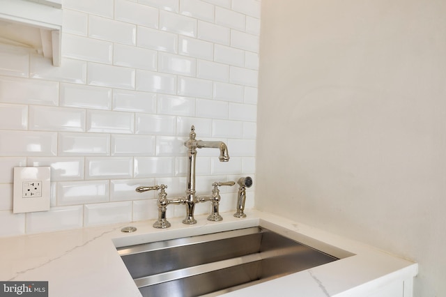 kitchen view of a sink, white cabinets, light stone countertops, and tasteful backsplash