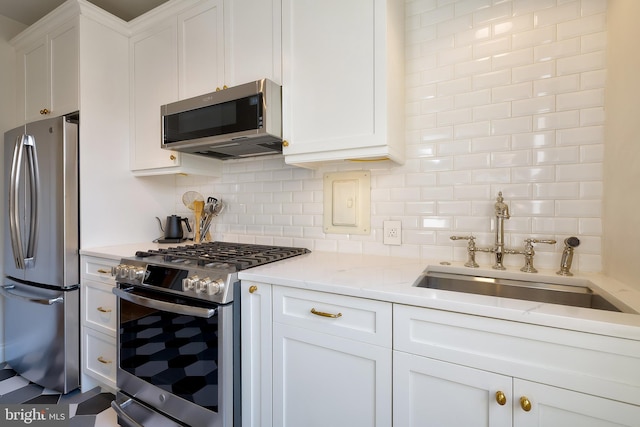 kitchen featuring stainless steel appliances, a sink, white cabinetry, and tasteful backsplash