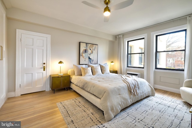bedroom with light wood-style floors, baseboards, a wall unit AC, and ceiling fan