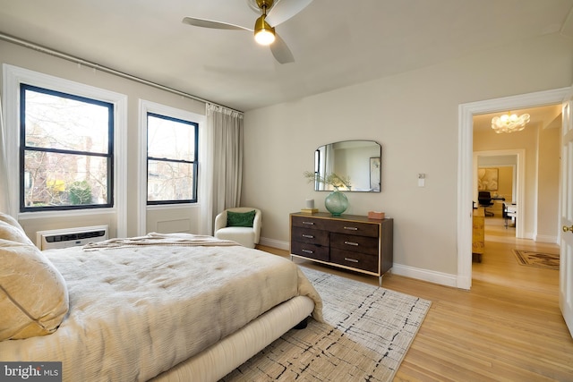 bedroom featuring light wood-type flooring, baseboards, a ceiling fan, a chandelier, and a wall mounted AC