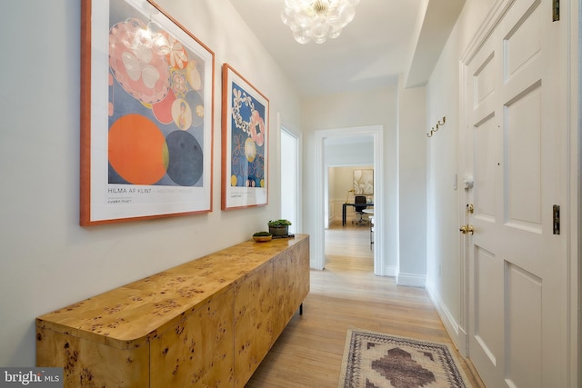 corridor with light wood finished floors, a chandelier, and baseboards