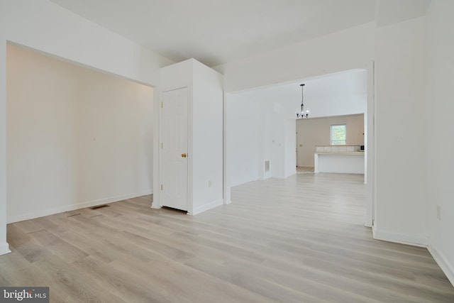 unfurnished room with a chandelier, light wood-style flooring, and baseboards