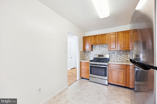 kitchen featuring appliances with stainless steel finishes, light countertops, brown cabinetry, decorative backsplash, and baseboards
