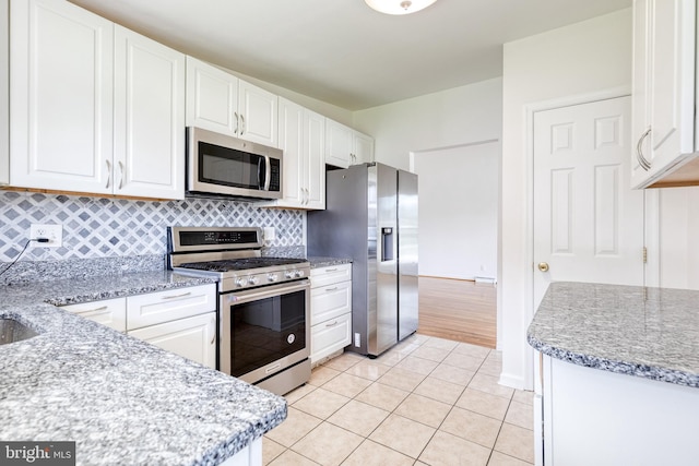 kitchen featuring appliances with stainless steel finishes, white cabinets, decorative backsplash, light tile patterned floors, and light stone counters