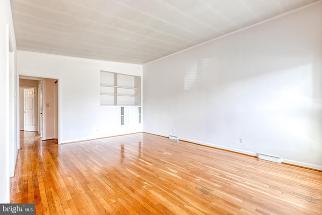 spare room featuring built in shelves, light wood-type flooring, and baseboards