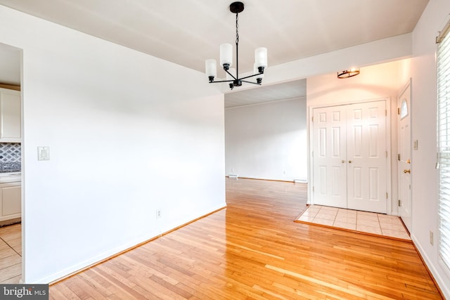 unfurnished dining area with a chandelier, light wood finished floors, and baseboards