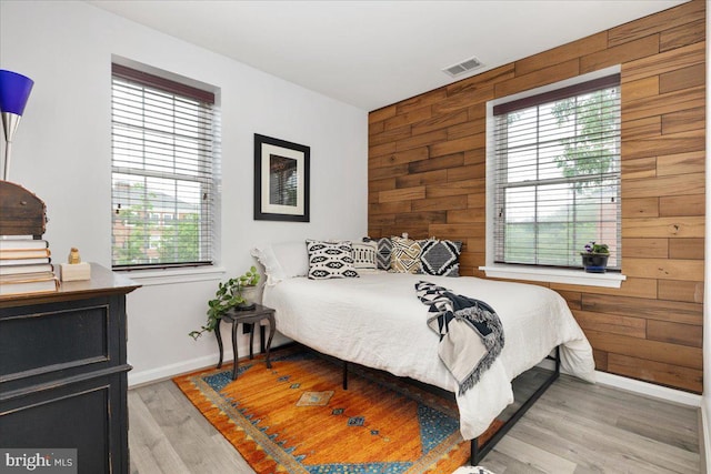 bedroom featuring wood walls, baseboards, multiple windows, and light wood-style flooring