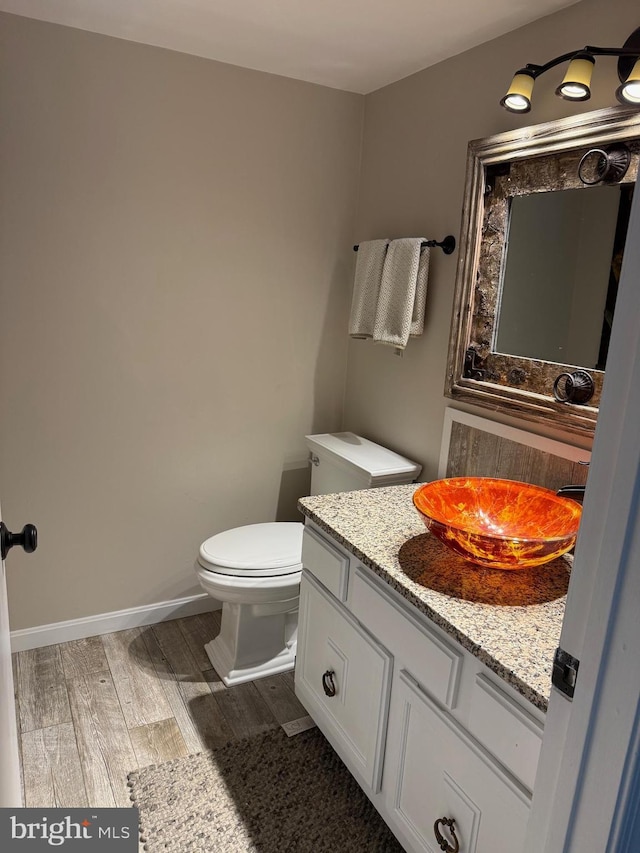 half bathroom featuring wood finished floors, toilet, vanity, and baseboards