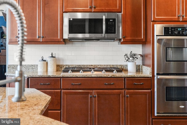 4108 Brushfield Dr, Frederick, MD 21704 - kitchen featuring stainless steel appliances, backsplash, light stone countertops, and brown cabinets