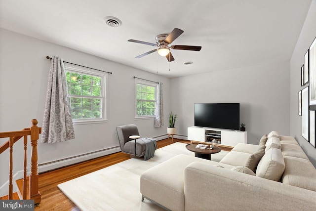 living area featuring a baseboard heating unit, wood finished floors, ceiling fan, and baseboards