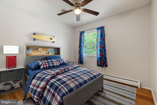 bedroom featuring a baseboard heating unit, wood finished floors, baseboards, and a ceiling fan