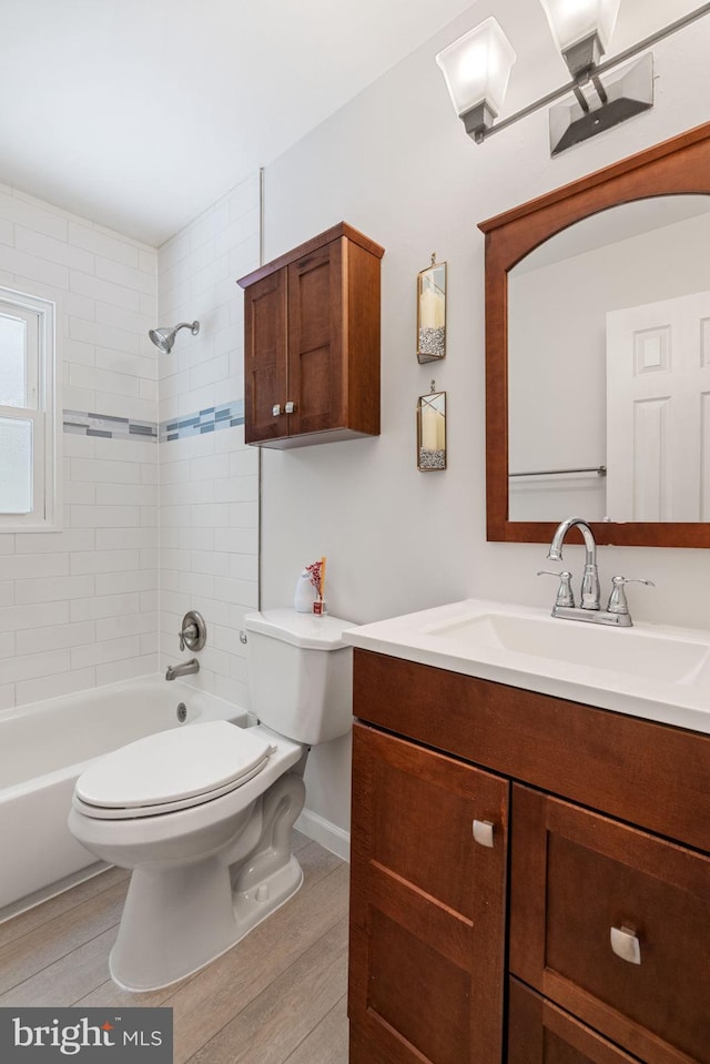 bathroom with toilet, wood finished floors, vanity, and  shower combination