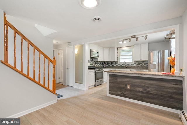 kitchen featuring appliances with stainless steel finishes, white cabinetry, backsplash, a sink, and a baseboard heating unit