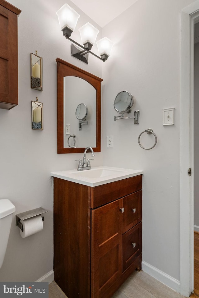 half bathroom with baseboards, vanity, and toilet