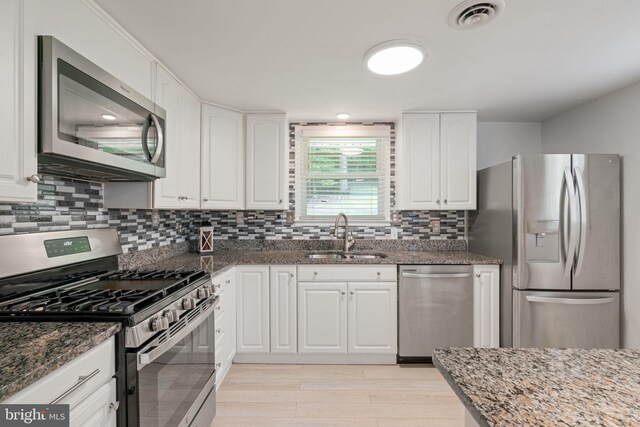 kitchen with stainless steel appliances, a sink, dark stone counters, white cabinetry, and tasteful backsplash