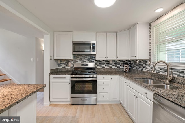kitchen featuring appliances with stainless steel finishes, a sink, light wood-style flooring, dark stone countertops, and decorative backsplash