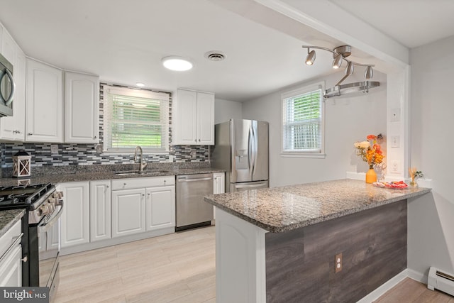 kitchen featuring stainless steel appliances, baseboard heating, a sink, dark stone counters, and white cabinetry