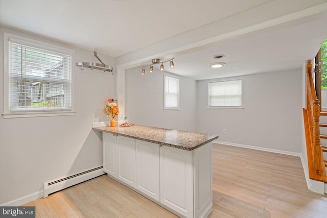 kitchen featuring baseboard heating, a peninsula, light wood-type flooring, white cabinets, and baseboards