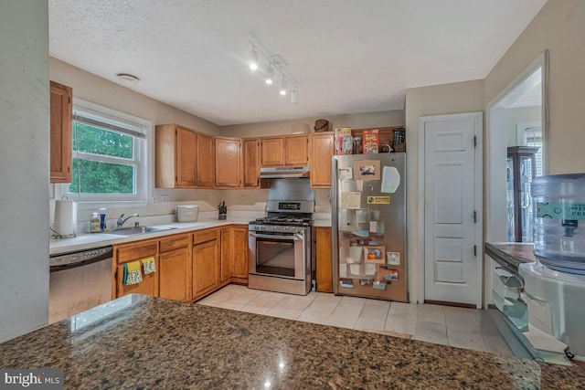 kitchen with stainless steel appliances, under cabinet range hood, a sink, and light tile patterned flooring