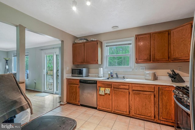 kitchen featuring appliances with stainless steel finishes, a sink, healthy amount of natural light, brown cabinets, and a textured ceiling