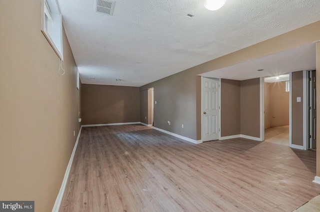 finished below grade area featuring light wood finished floors, baseboards, and a textured ceiling
